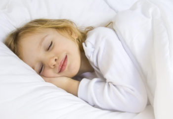 Little blond girl wearing white blouse in white bedchlothes