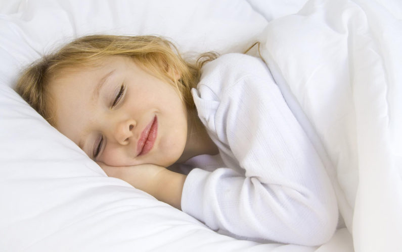 Little blond girl wearing white blouse in white bedchlothes