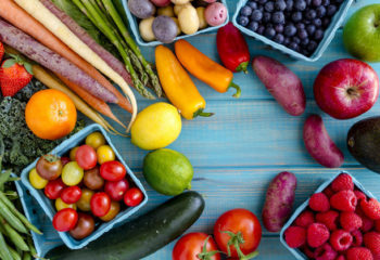 Variety of fresh raw organic fruits and vegetables in light blue containers sitting on bright blue wooden background