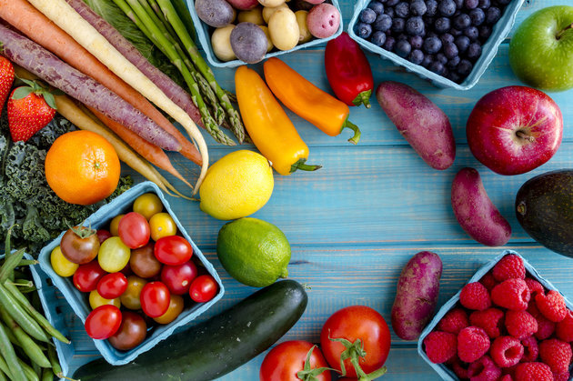 Variety of fresh raw organic fruits and vegetables in light blue containers sitting on bright blue wooden background